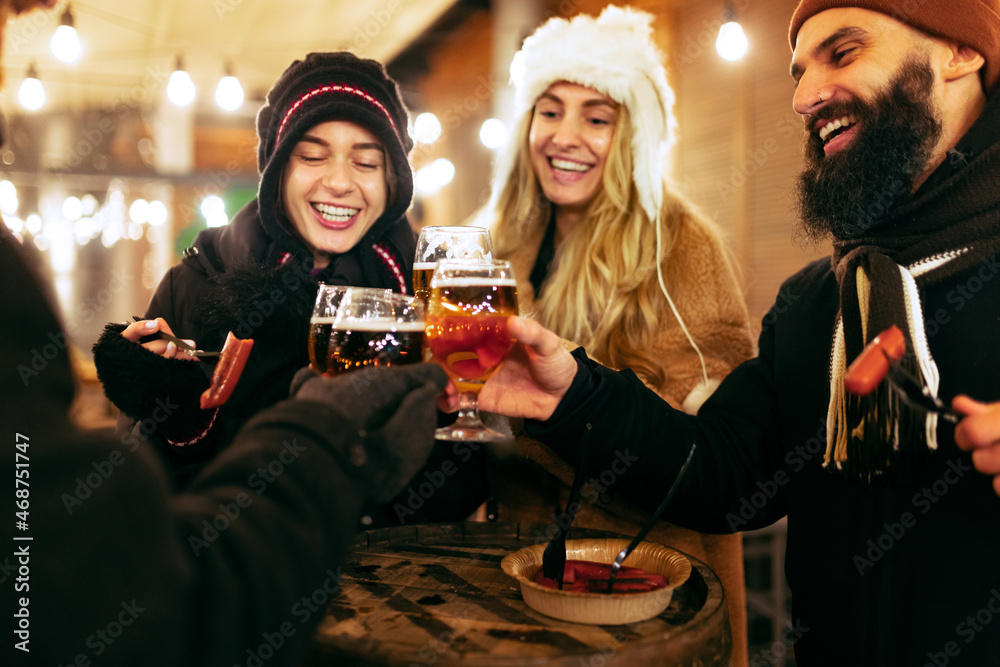 Close-up happy smiling friends with cups of mulled wine spending time together at winter fair at evening. Holidays, Christmas concept Close-up happy smiling friends with cups of mulled wine spending time together at winter fair at evening. Holidays, Christmas concept