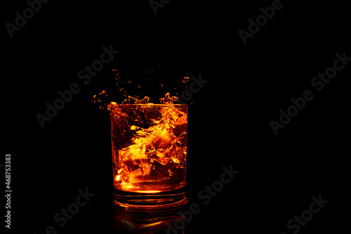 glass with brown liquid with ice cubes and bottom illumination on dark background