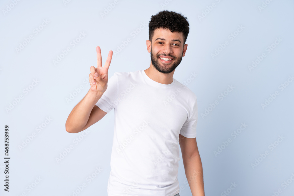 Young Moroccan man isolated on blue background smiling and showing victory sign