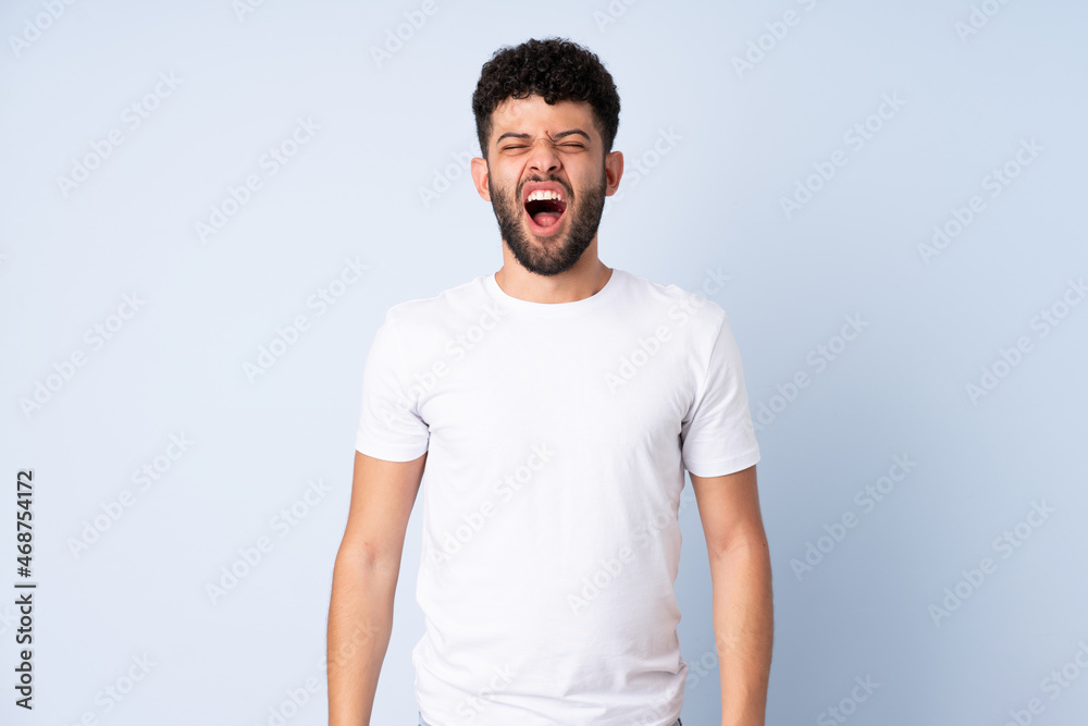 Young Moroccan man isolated on blue background shouting to the front with mouth wide open Young Moroccan man isolated on blue background shouting to the front with mouth wide open