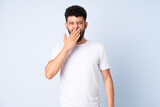 Young Moroccan man isolated on blue background yawning and covering wide open mouth with hand
