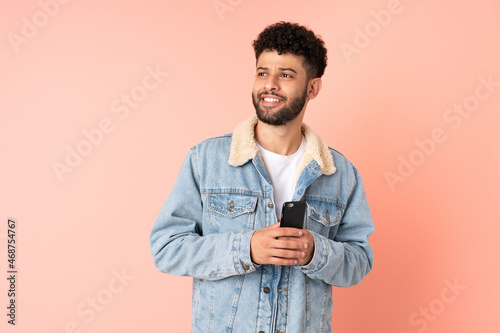 Young Moroccan man using mobile phone isolated on pink background thinking an idea while looking up © luismolinero