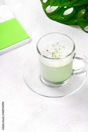 Matcha latte with foam on plant-based milk in glass cup on the white desk. Hot healthy drink 