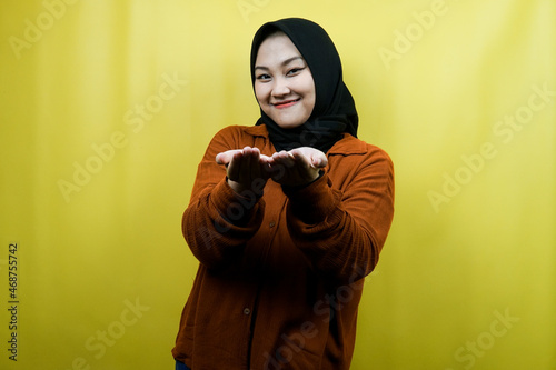 Beautiful and cheerful young asian muslim woman, with open arms, presenting something happily, isolated