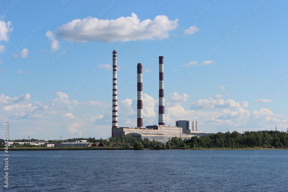 Volga River in summer, view from the middle of the river to an industrial enterprise on the shore with three tall pipes
