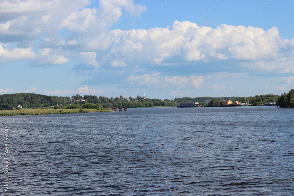 Volga River in summer, view from the ship - calm current, blue sky with clouds, the shore in the distance