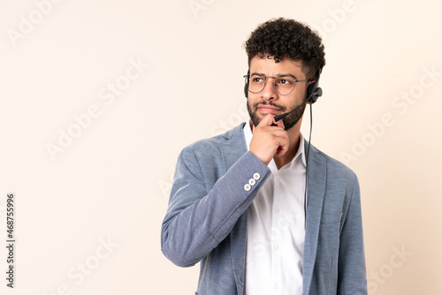 Telemarketer Moroccan man working with a headset isolated on beige background and looking up