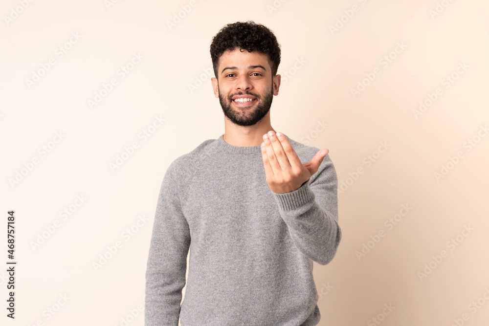 Young Moroccan man isolated on beige background inviting to come with hand. Happy that you came Young Moroccan man isolated on beige background inviting to come with hand. Happy that you came
