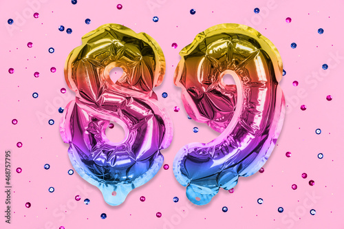 Rainbow foil balloon number, digit eighty nine on a pink background with sequins. Birthday greeting card with inscription 89. Top view. Numerical digit. Celebration event, template. photo