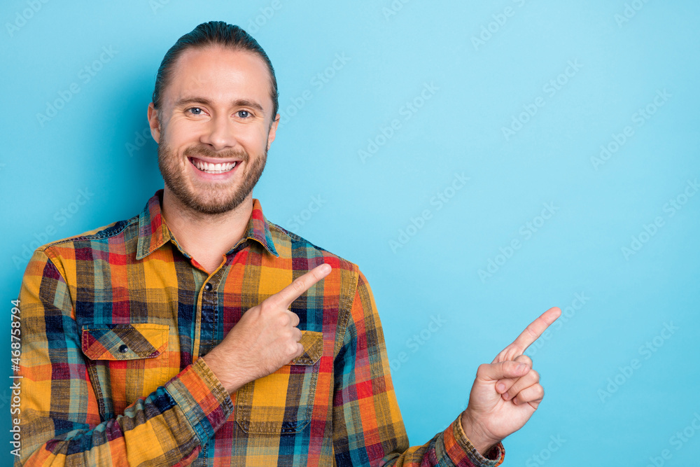 Photo of optimistic young brunette guy indicate empty space wear yellow shirt isolated on blue color background