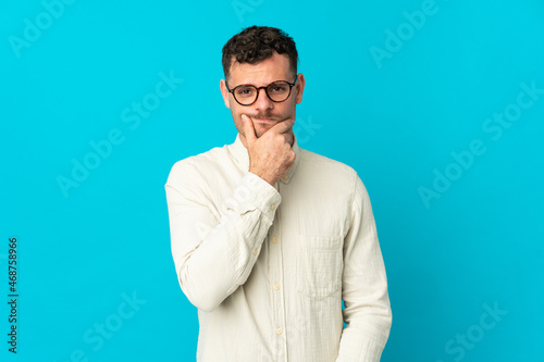 Young caucasian handsome man isolated on blue background having doubts © luismolinero