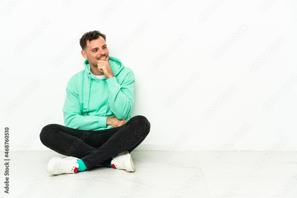 Young handsome caucasian man sitting on the floor looking to the side Young handsome caucasian man sitting on the floor looking to the side