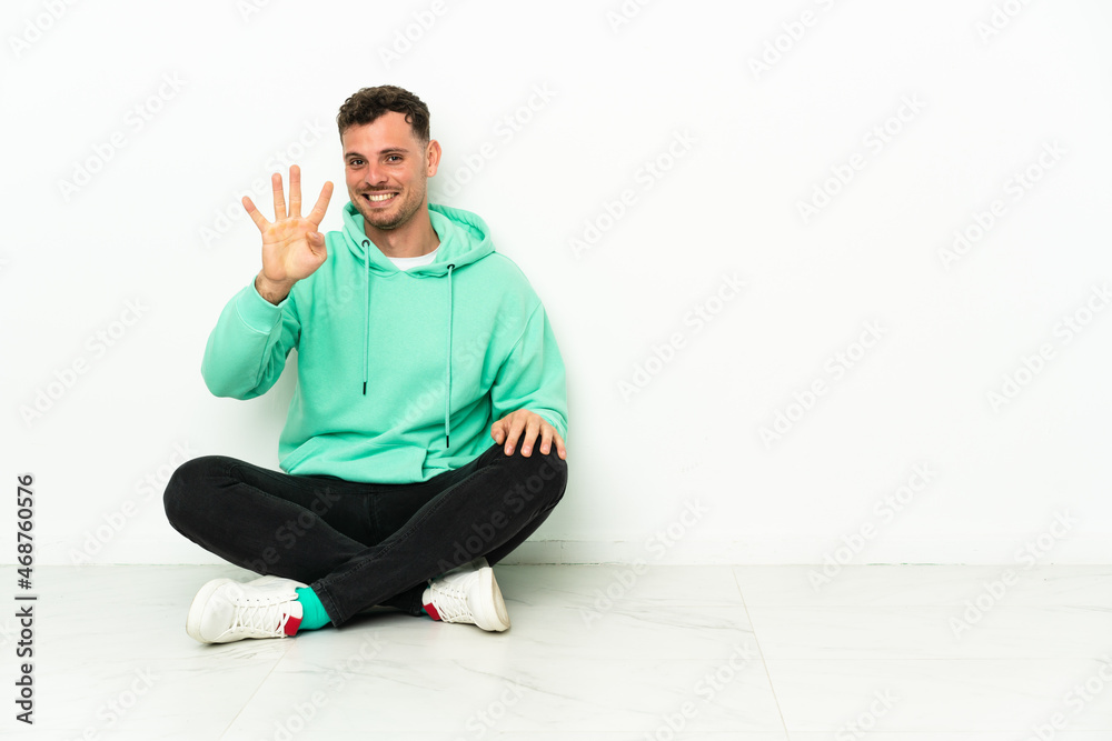 Young handsome caucasian man sitting on the floor happy and counting four with fingers Young handsome caucasian man sitting on the floor happy and counting four with fingers