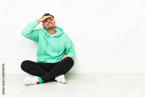 Young handsome caucasian man sitting on the floor looking far away with hand to look something