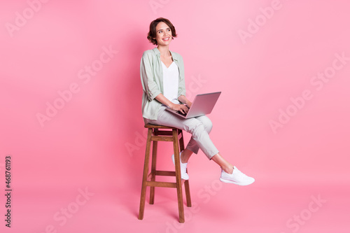 Full length photo of bob hairdo millennial lady sit laptop look empty space wear grey green look isolated on pink background