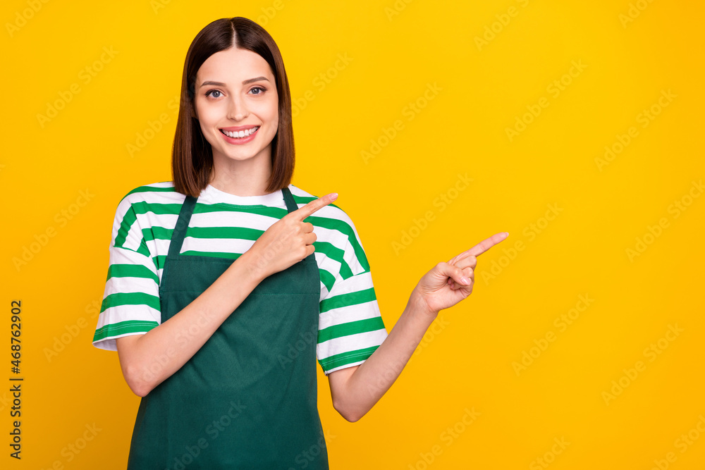 Photo of optimistic brunette millennial waitress lady index empty space wear apron striped t-shirt isolated on yellow color background Photo of optimistic brunette millennial waitress lady index empty space wear apron striped t-shirt isolated on yellow color background