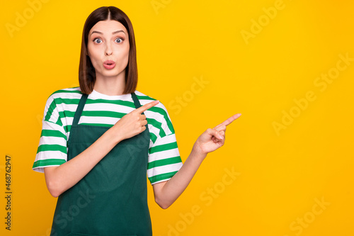 Photo of impressed brunette young working lady indicate empty space wear apron green t-shirt isolated on yellow color background