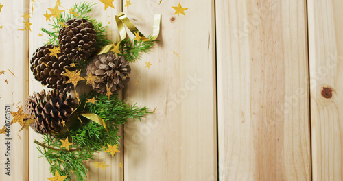 Image of stars falling over pine cones and wooden background with copy space