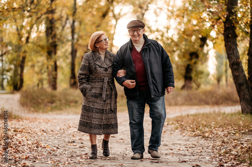 Attractive and happy couple of married people slowly walking autumn park, enjoying fresh air and rustle of foliage, lady looking with love on her man, happy old age together, family