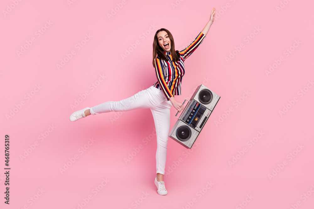 Fototapeta premium Photo of impressed funky young lady wear striped shirt dancing holding boom box smiling isolated pink color background