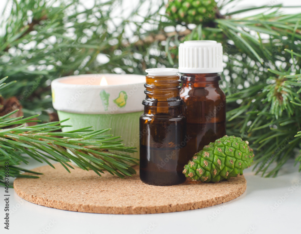 Small glass bottles with essential pine oil, pine branches, green cone and burning candle. Aromatherapy, sauna, homemade spa and herbal medicine ingredients. Copy space. Small glass bottles with essential pine oil, pine branches, green cone and burning candle. Aromatherapy, sauna, homemade spa and herbal medicine ingredients. Copy space.