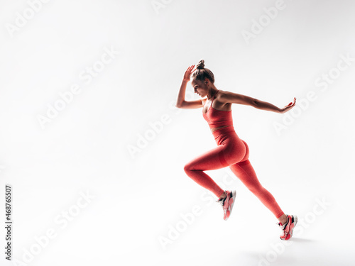Fitness confident woman in pink sports clothing. Young beautiful model with perfect body. Female isolated on white in studio. Cheerful and happy. Jumping and running