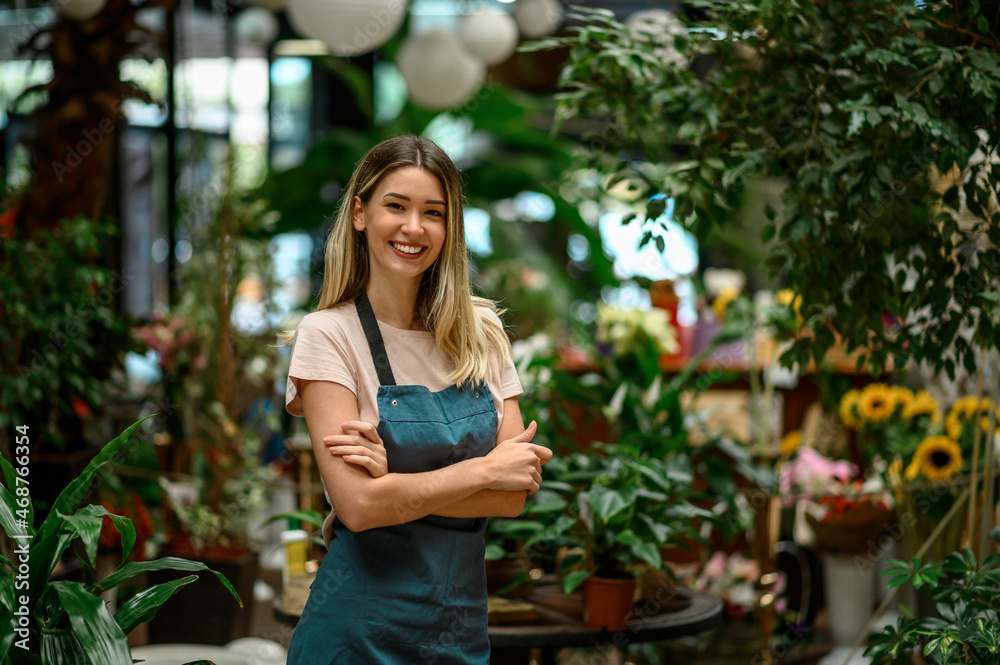 Florist working in flower shop while smiling and looking at a camera Florist working in flower shop while smiling and looking at a camera