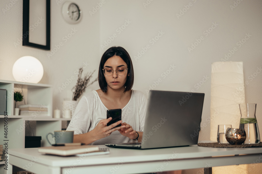 Beautiful woman using smartphone and a laptop while working from home Beautiful woman using smartphone and a laptop while working from home