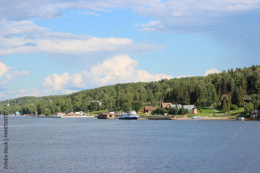 Volga River in summer - the vicinity of the city of Ples, view from the ship. Houses and other buildings on the shore between the trees. Volga River in summer - the vicinity of the city of Ples, view from the ship. Houses and other buildings on the shore between the trees.