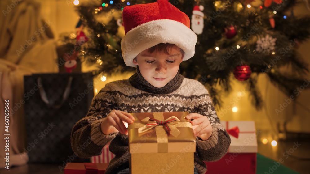Portrait of amazed and excited boy in Santa hat looking inside Christmas present box. Families and children celebrating winter holidays.