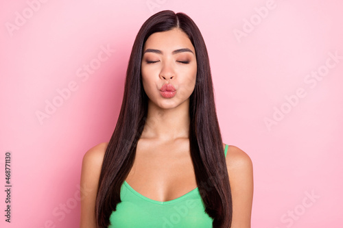 Photo of adorable sweet young woman dressed green singlet closed eyes sending you kiss isolated pink color background