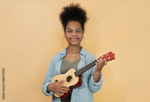Happy cute kid girl with afro hair and ukulele on yellow background