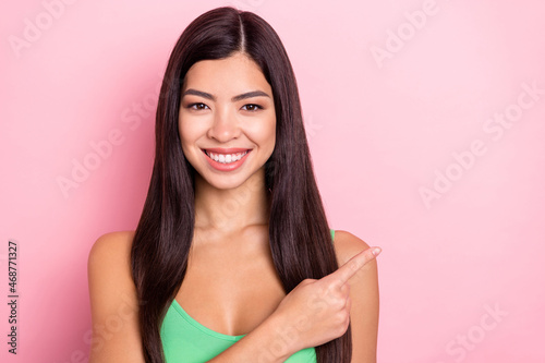 Photo of funny charming young woman dressed green singlet smiling pointing finger empty space isolated pink color background