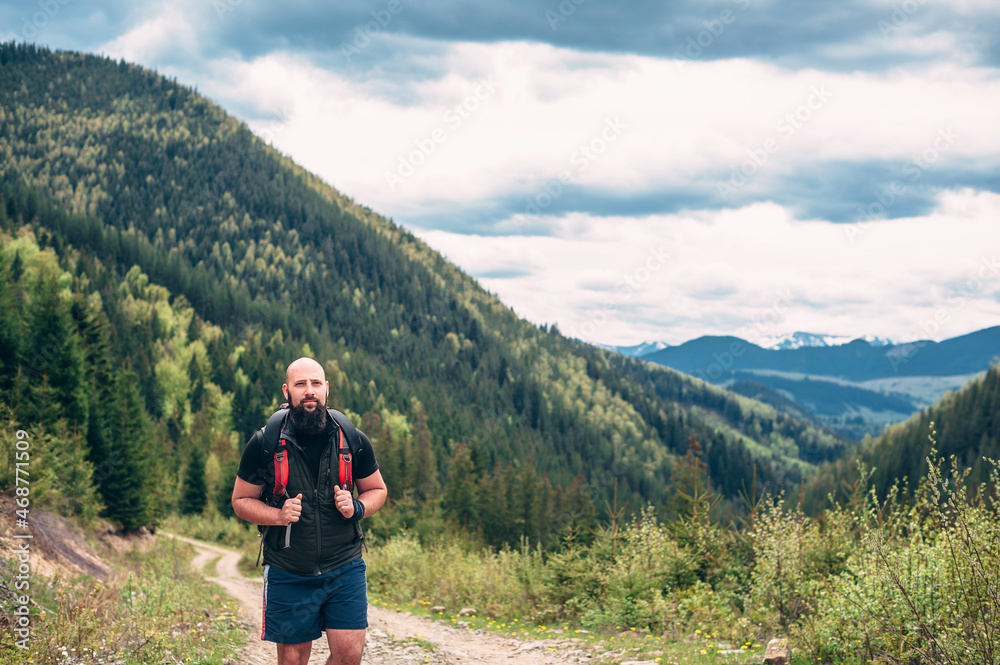 Caucasian man with backpack hiking on a trail in the rocky mountains. A handsome bearded man 30 years old walks along the trail against the background of a pine forest.