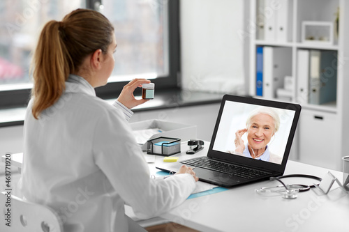 healthcare, technology and medicine concept - female doctor with laptop computer having video call with patient and showing drug jar at hospital