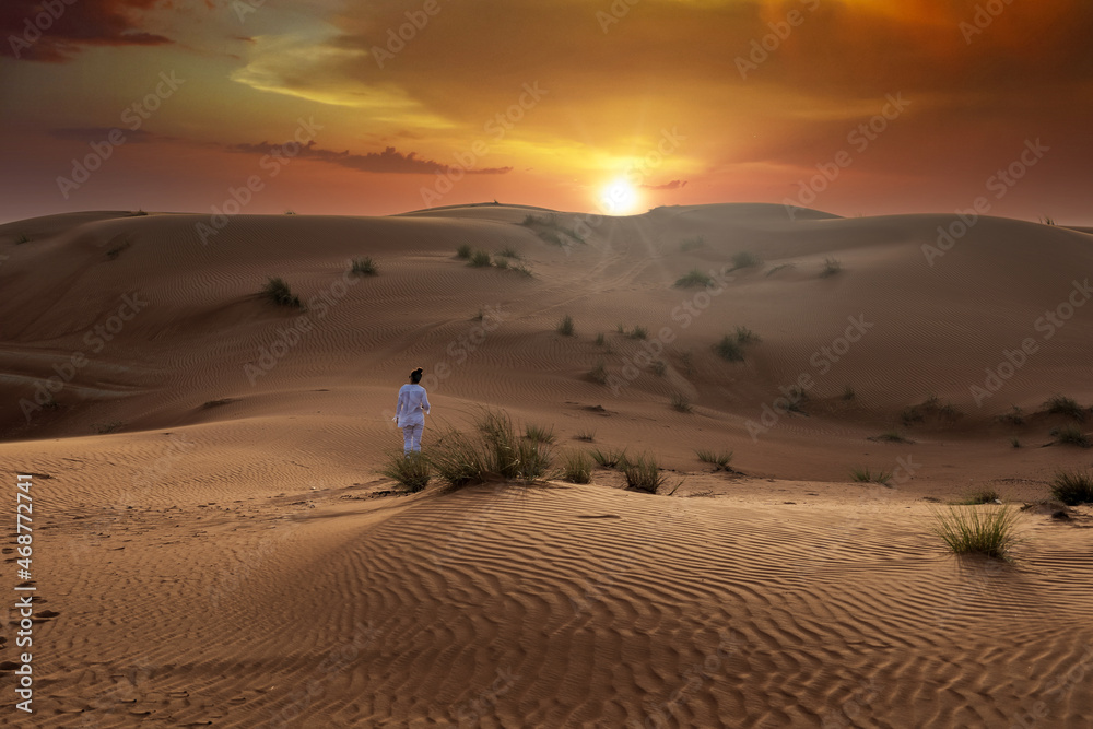 Beautiful desert landscape during sunset and golden hour with very dramatic sky with a person walking between dunes