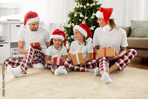 family, winter holidays and people concept - happy mother, father and two daughters in santa hats with christmas gifts at home