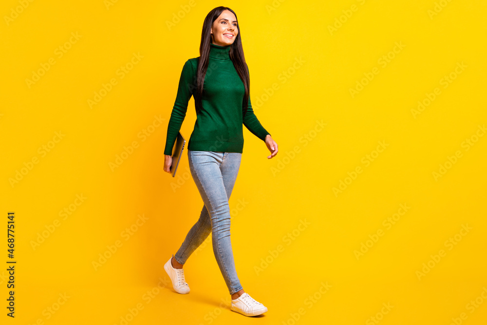 Full length photo of cheerful happy young woman walk empty space hold laptop isolated on yellow color background