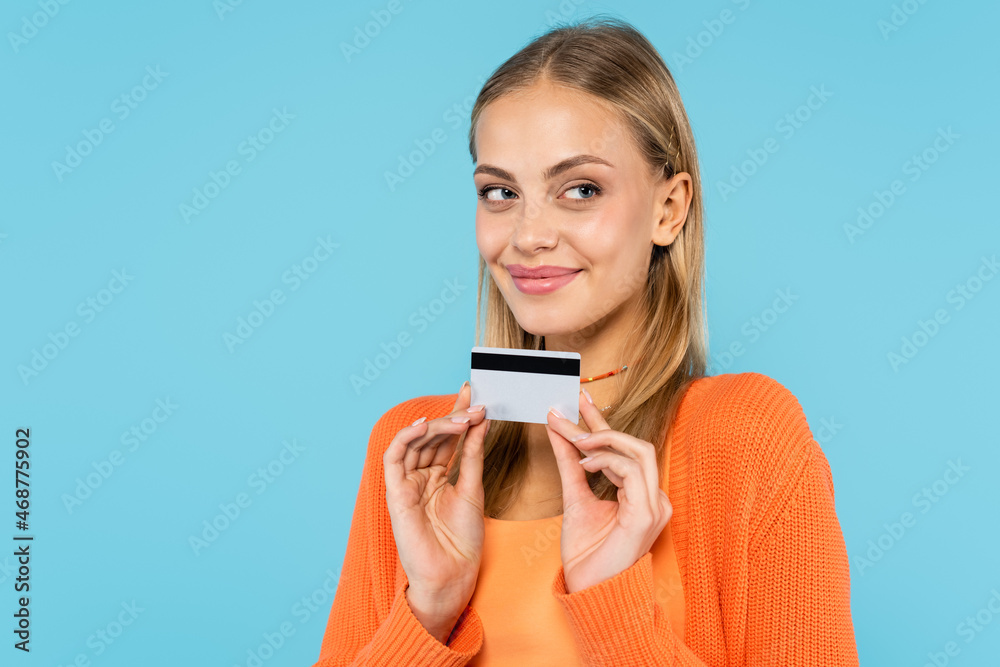 Pretty blonde woman holding credit card and looking away isolated on blue Pretty blonde woman holding credit card and looking away isolated on blue