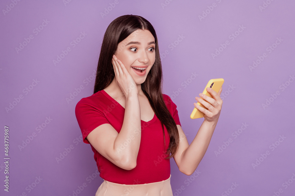 Portrait of positive excited cheerful lady hold phone palm cheek look screen on violet background Portrait of positive excited cheerful lady hold phone palm cheek look screen on violet background
