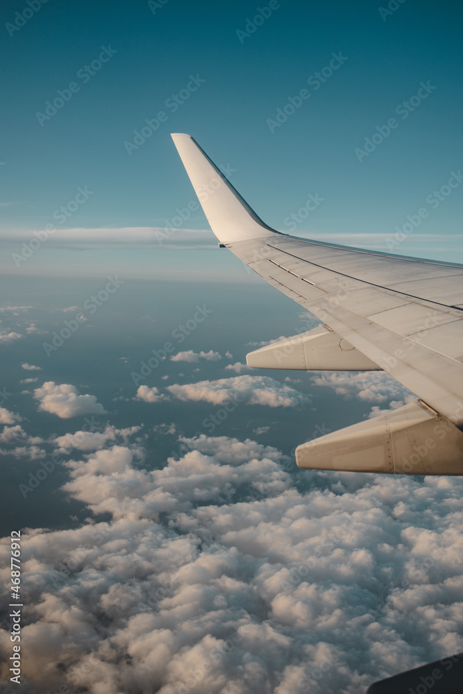 Vertical shot of the wing of the airplane over the cloudy blue sky Vertical shot of the wing of the airplane over the cloudy blue sky