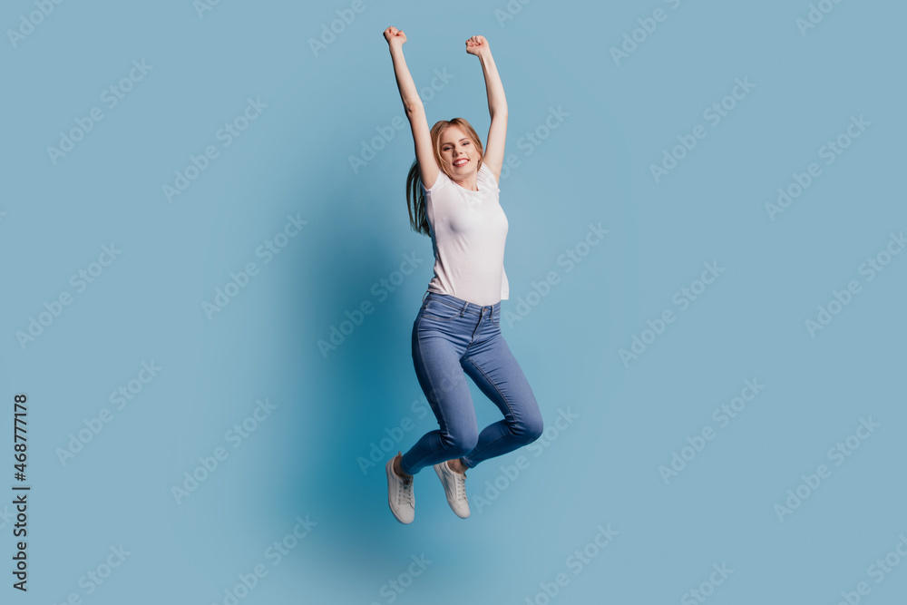 Photo of cheerful astonished funny champion lady jump raise fists wear casual clothes on blue color background