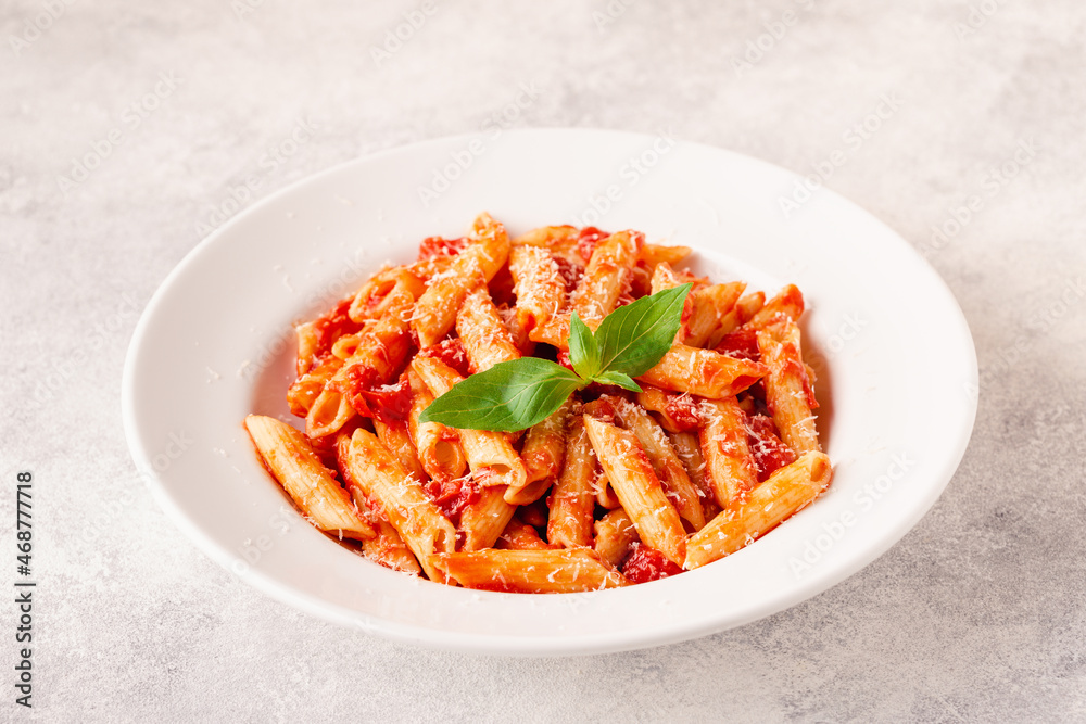 Classic italian pasta penne alla arrabiata with fresh basil on a light background Classic italian pasta penne alla arrabiata with fresh basil on a light background