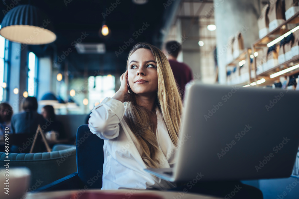 Thoughtful female freelancer working on laptop in cafeteria