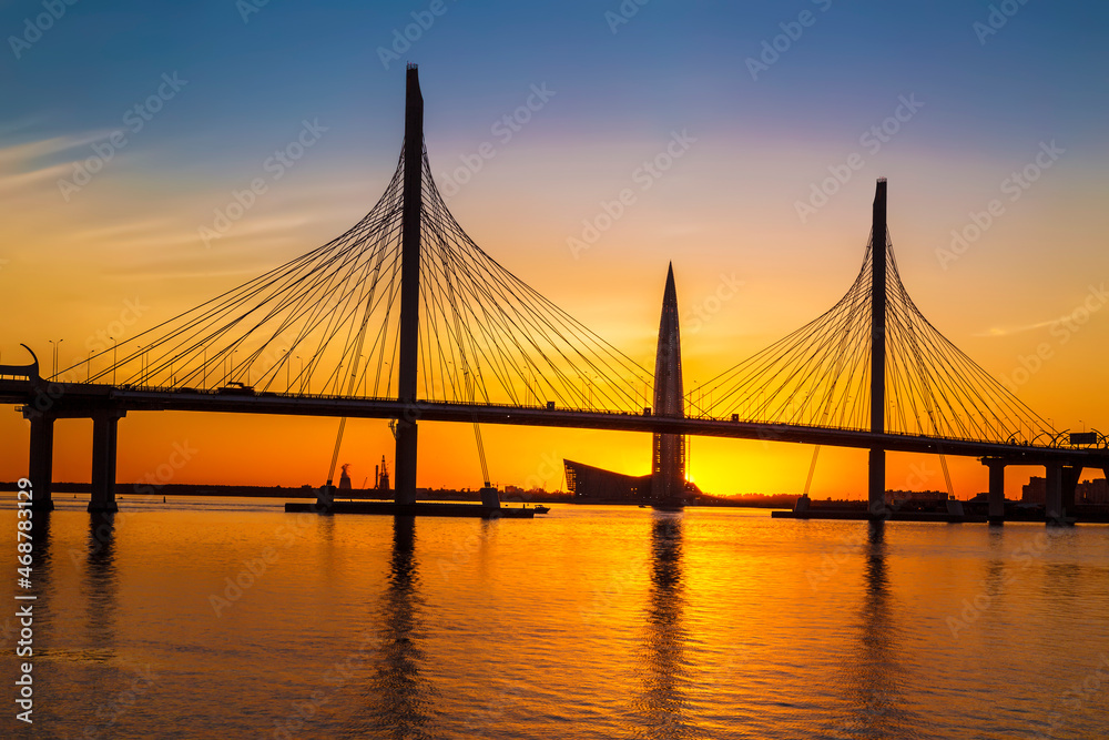 Fototapeta premium View of the cable-stayed bridge of the western high-speed diameter across the Malaya Neva River and the silhouette of the Lakhta Center building at sunset. Saint Petersburg, Russia