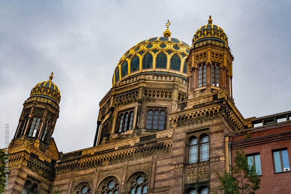 Great close-up view of the New Synagogue's main dome in Berlin, with its gilded ribs, flanked by two smaller pavilion-like domes on the two side-wings on a cloudy day.