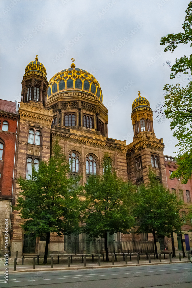 Obraz premium Nice view of the New Synagogue on the street Oranienburger Straße in Berlin, Germany on a cloudy day. The synagogue's main dome, with its gilded ribs, is an eye-catching landmark.