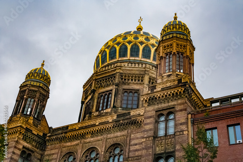 Great close-up view of the New Synagogue's main dome in Berlin, with its gilded ribs, flanked by two smaller pavilion-like domes on the two side-wings on a cloudy day.