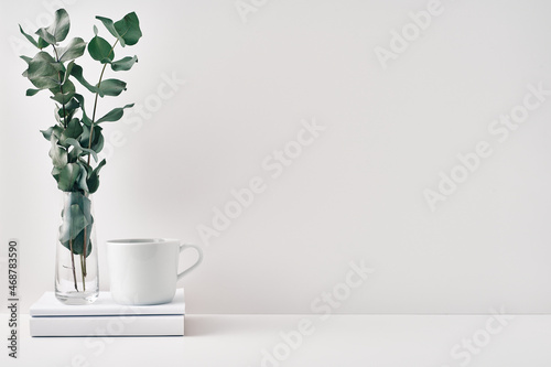 A mug  a stack of books  a wooden board and a transparent vase with eucalyptus branches. Eco-friendly materials in interior decor  minimalism. Copy space  mock up