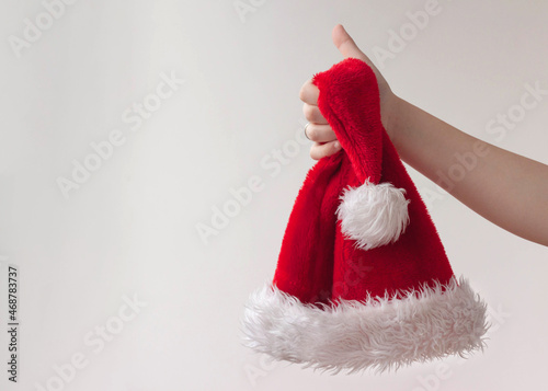 A hand holds out a red hat with white fur, Santa hat